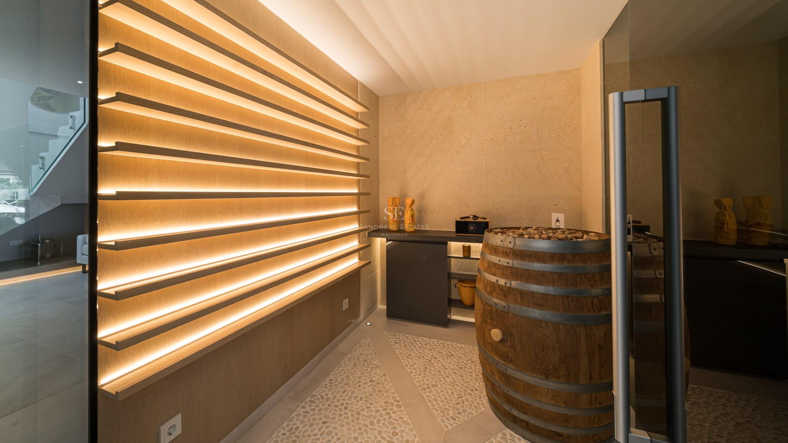 Modern wine cellar featuring backlit oak shelving, limestone walls, and a decorative wine barrel.