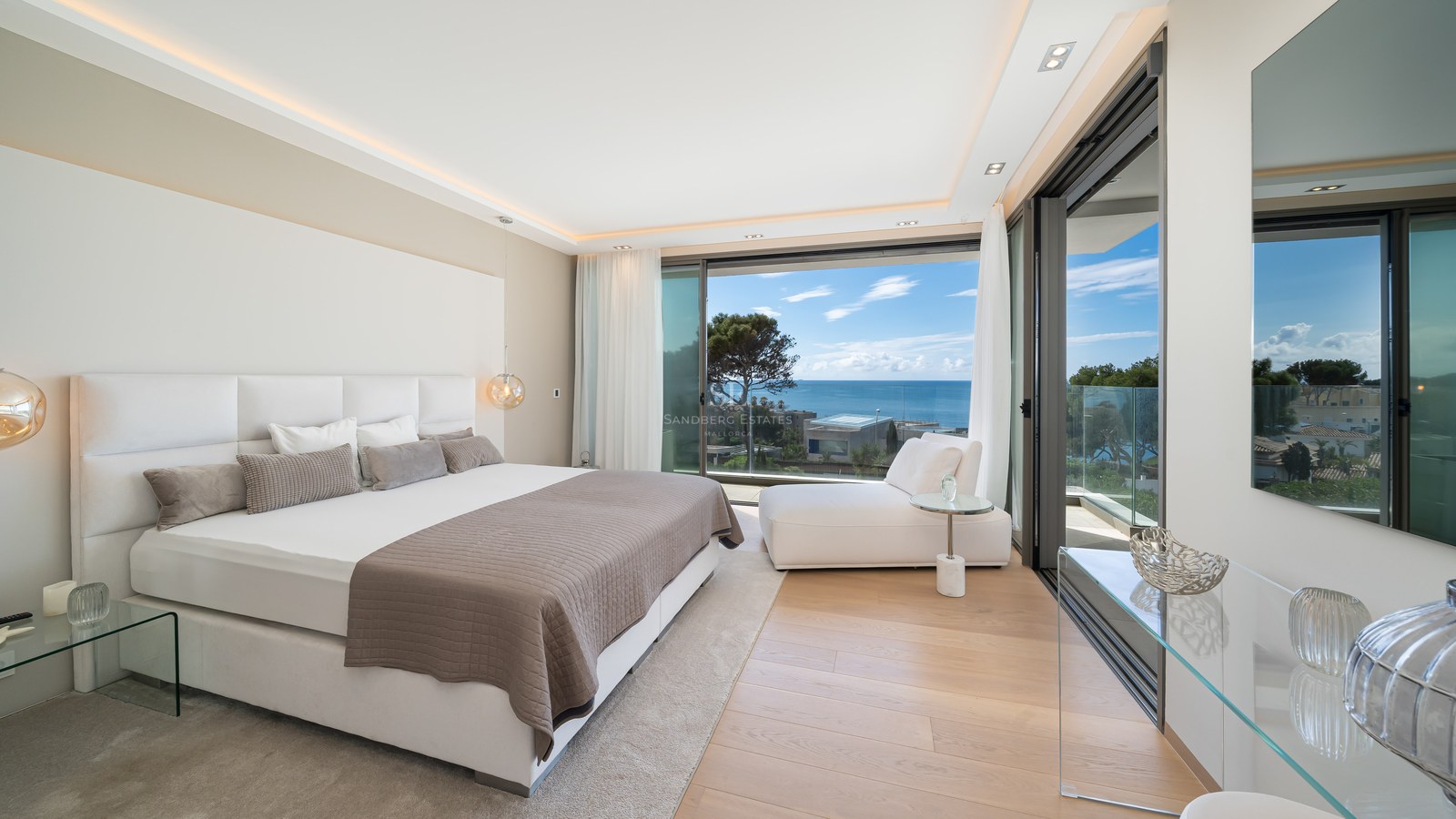 A contemporary master bedroom with a large bed, wooden floors, and floor-to-ceiling glass doors opening to a sea view.