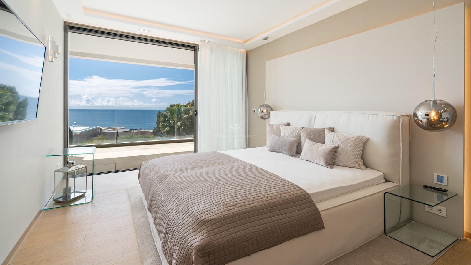 Modern master bedroom featuring white bedding and glass doors opening to a private terrace with Mediterranean Sea views.