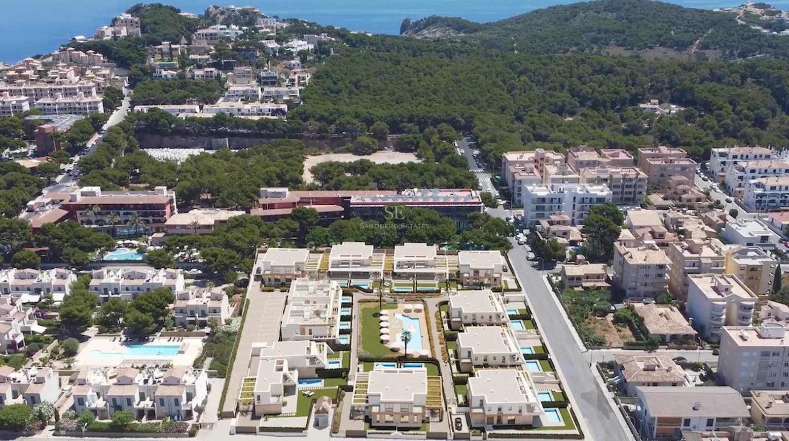 Drohnenaufnahme einer modernen Wohnanlage mit weißen Gebäuden, privaten Pools und üppiger mediterraner Vegetation.
