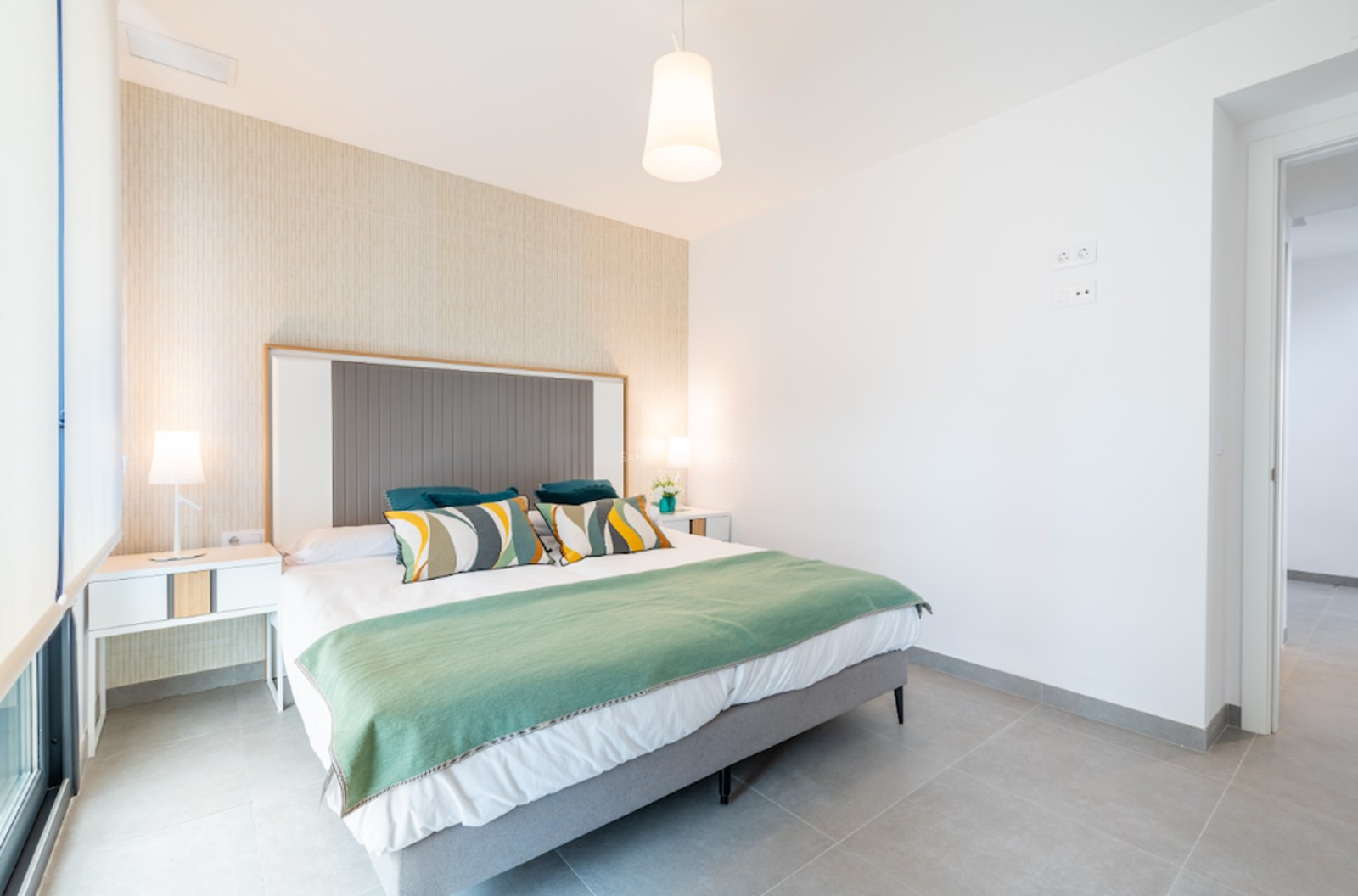 Modernes Schlafzimmer mit großem Bett, grüner Decke, strukturierter Akzentwand und zwei Nachttischlampen.