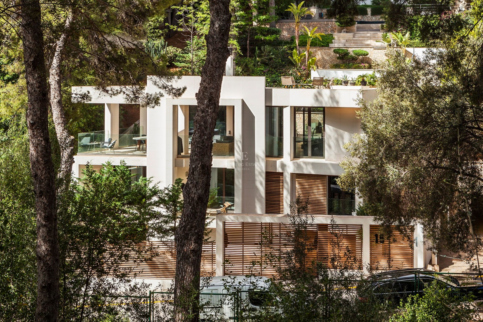 Villa contemporaine à plusieurs niveaux avec façade en pierre, lattes de bois et terrasses en verre entourée de pins.