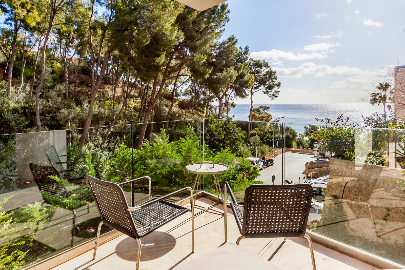 Terrasse avec garde-corps en verre et mobilier moderne donnant sur une pinède et la mer Méditerranée.