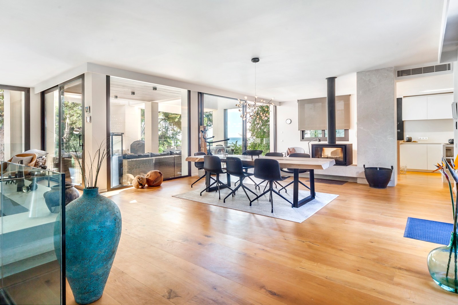 Salle à manger avec table en bois massif, chaises noires modernes, cheminée et baies vitrées ouvrant sur le jardin.