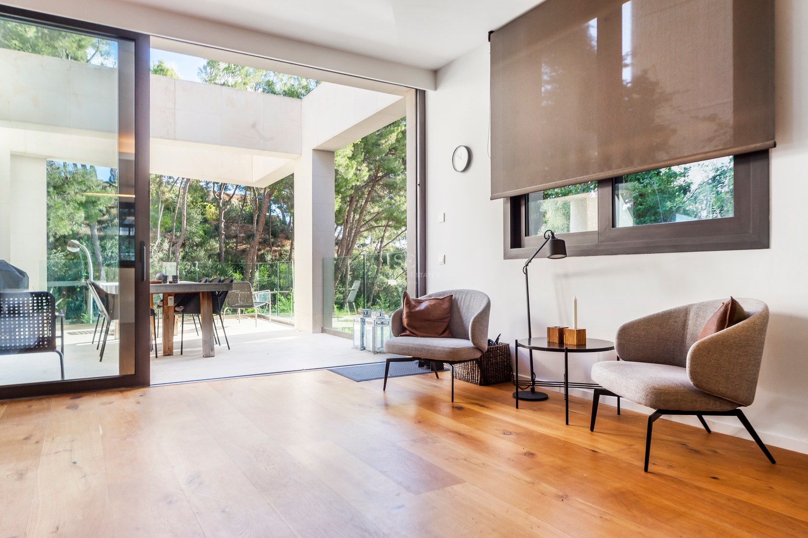Coin salon moderne avec deux fauteuils gris sur parquet en chêne, s'ouvrant sur une terrasse ensoleillée.