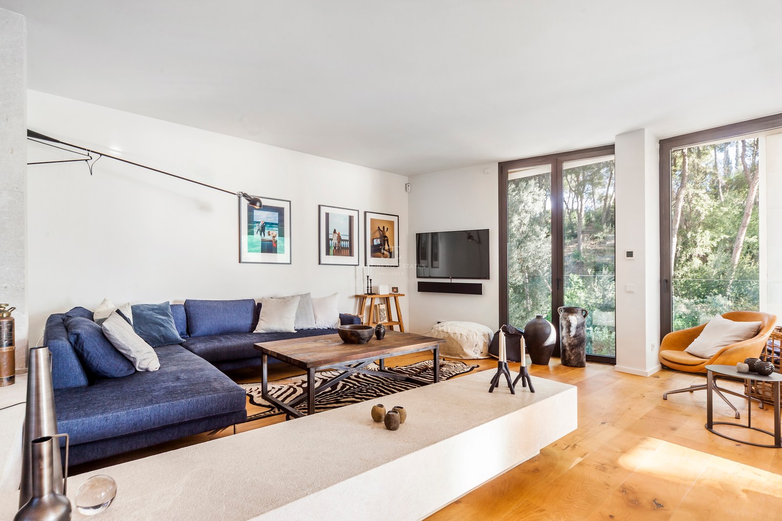 Salon moderne avec canapé bleu, parquet en chêne et grandes baies vitrées donnant sur une forêt.