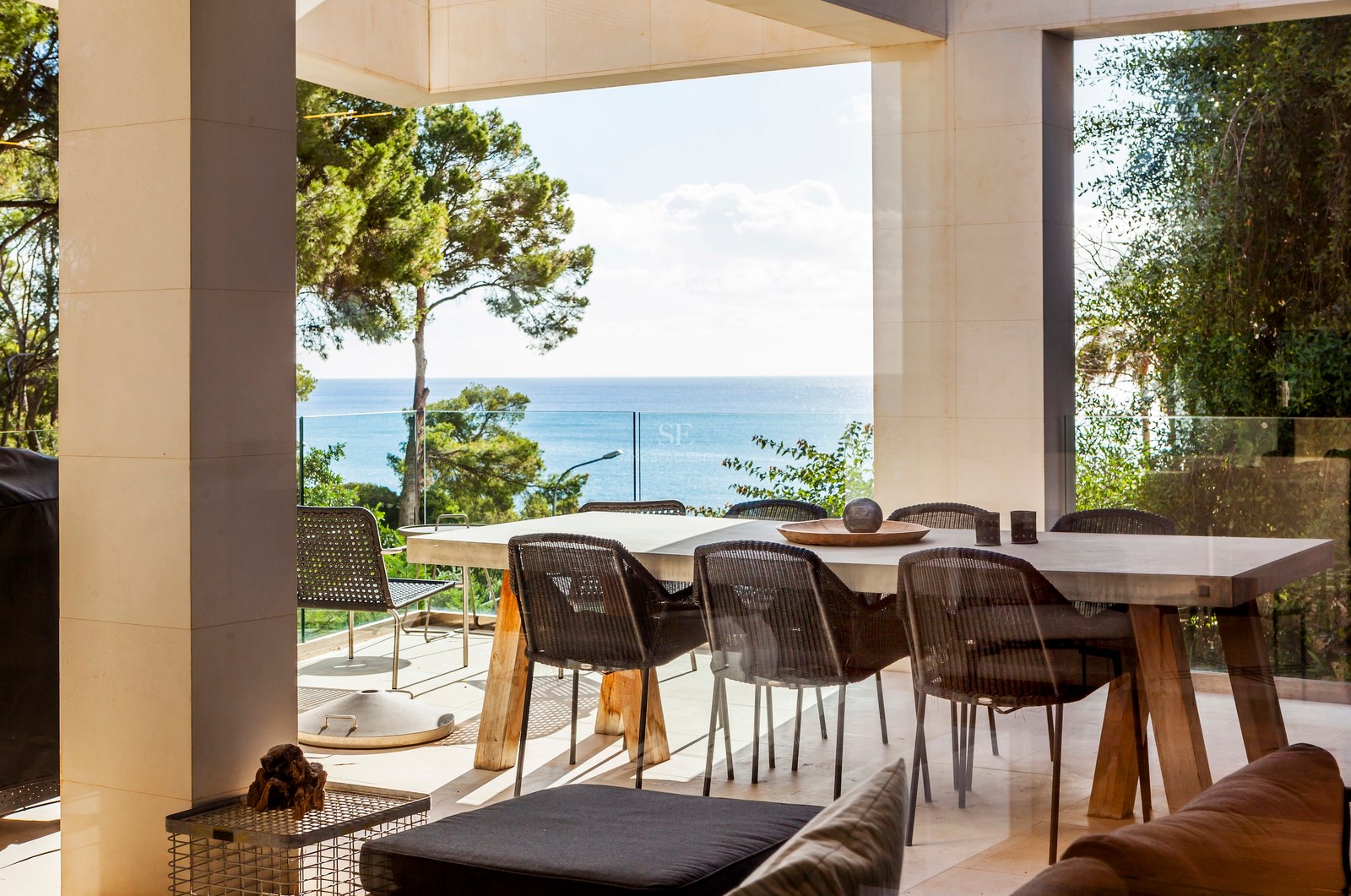Espace dînatoire extérieur sur une terrasse en pierre avec garde-corps en verre et vue sur la Méditerranée.