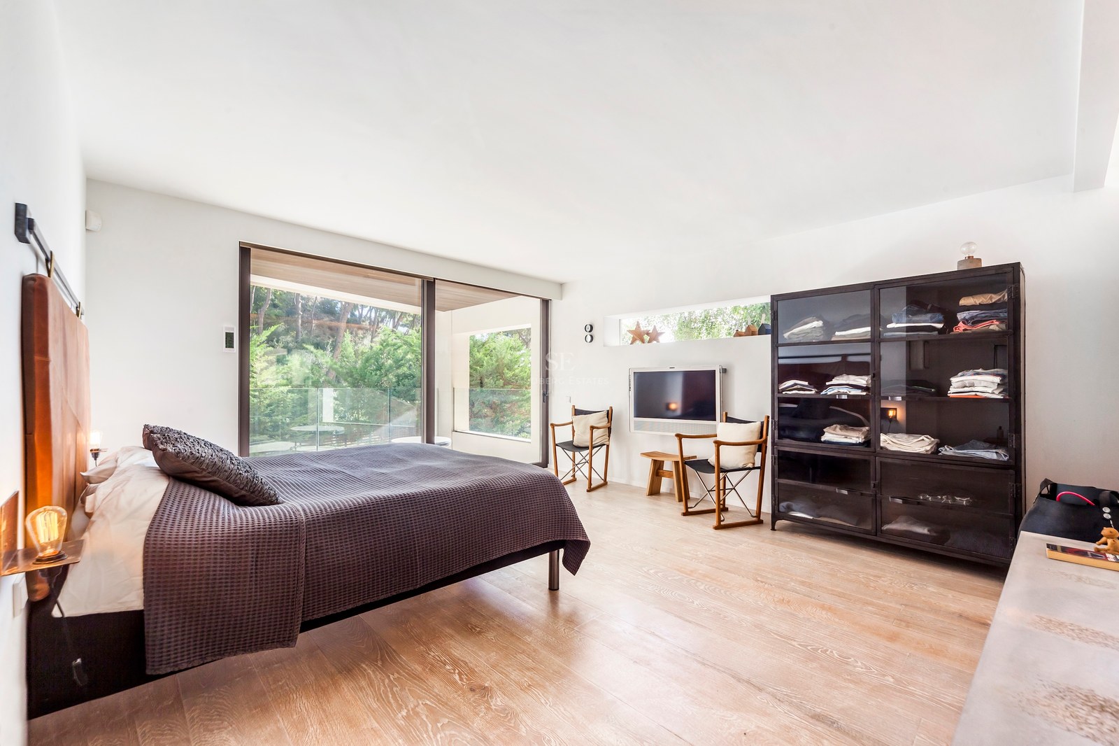 Chambre contemporaine lumineuse avec parquet en chêne, baies vitrées et armoire industrielle en verre noir.