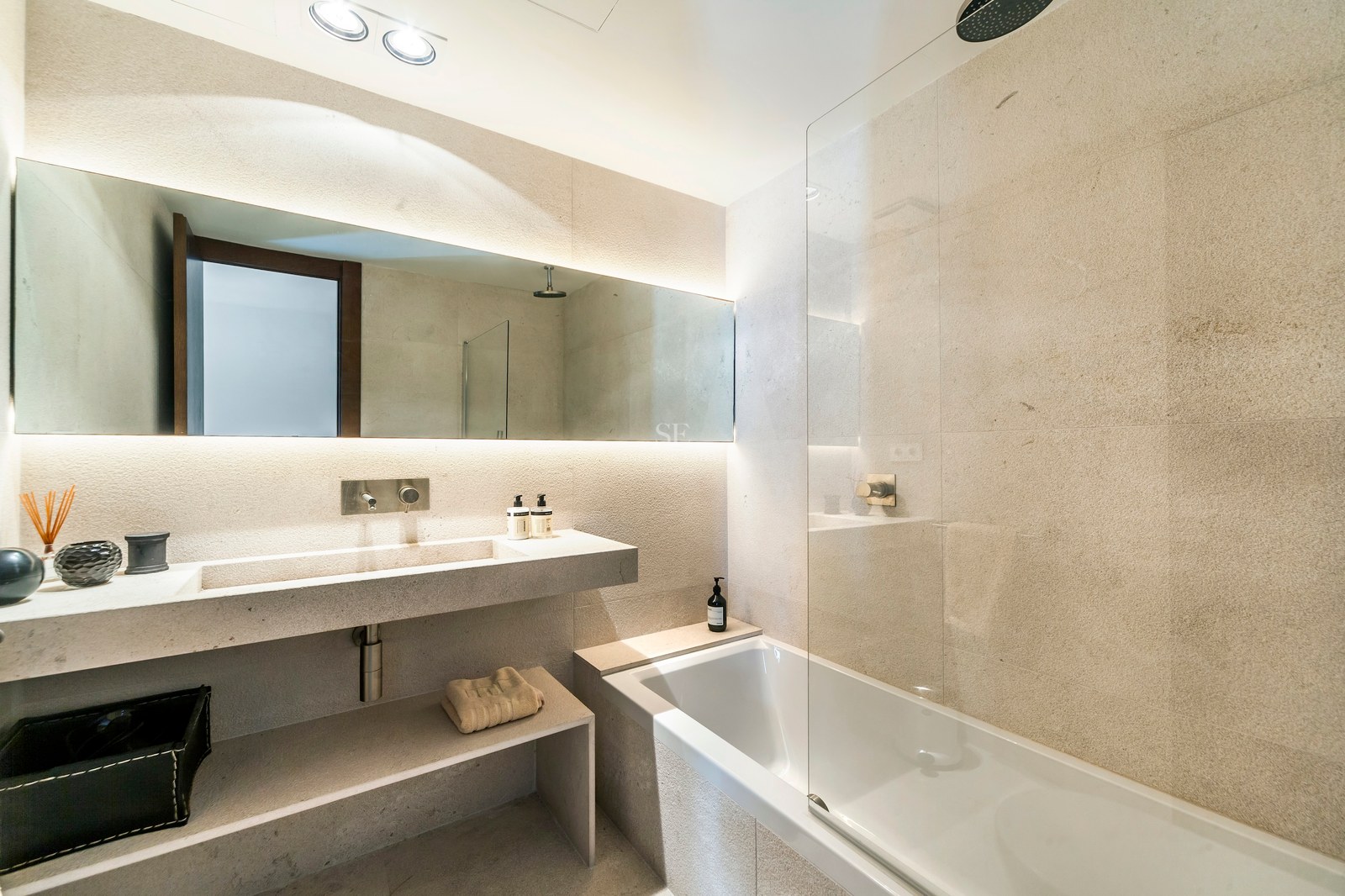 Salle de bains de luxe avec vasque en pierre, miroir rétroéclairé et baignoire avec paroi en verre.