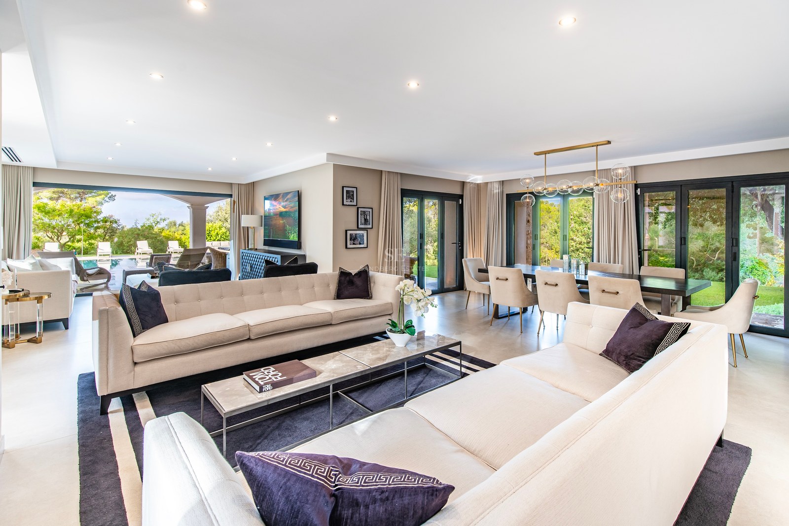 Salón espacioso y contemporáneo con sofás color crema, mesa de mármol y ventanales que dan al jardín.