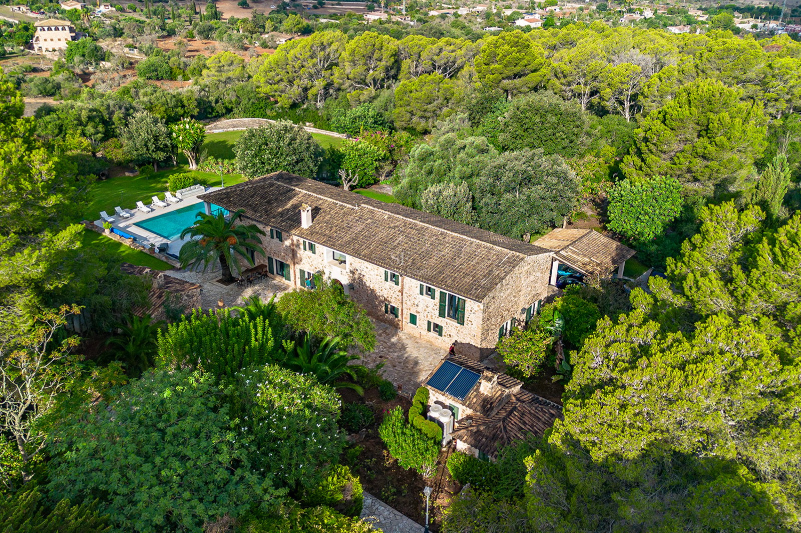 Vista aérea de una gran casa de campo de piedra y piscina rodeada de un denso bosque de pinos verdes.