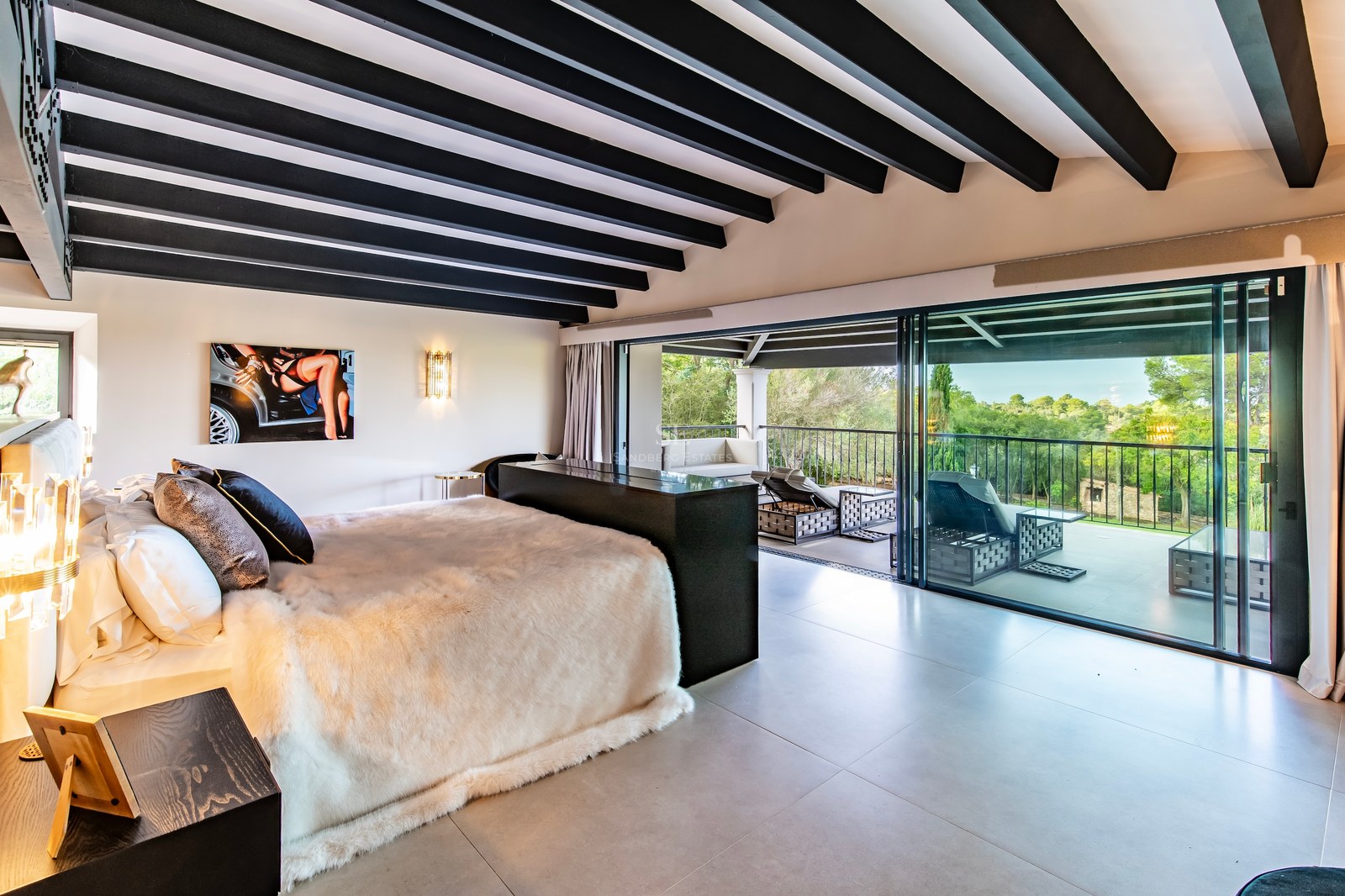 Dormitorio principal moderno con vigas oscuras y puertas de cristal que dan a una terraza con vistas al bosque.
