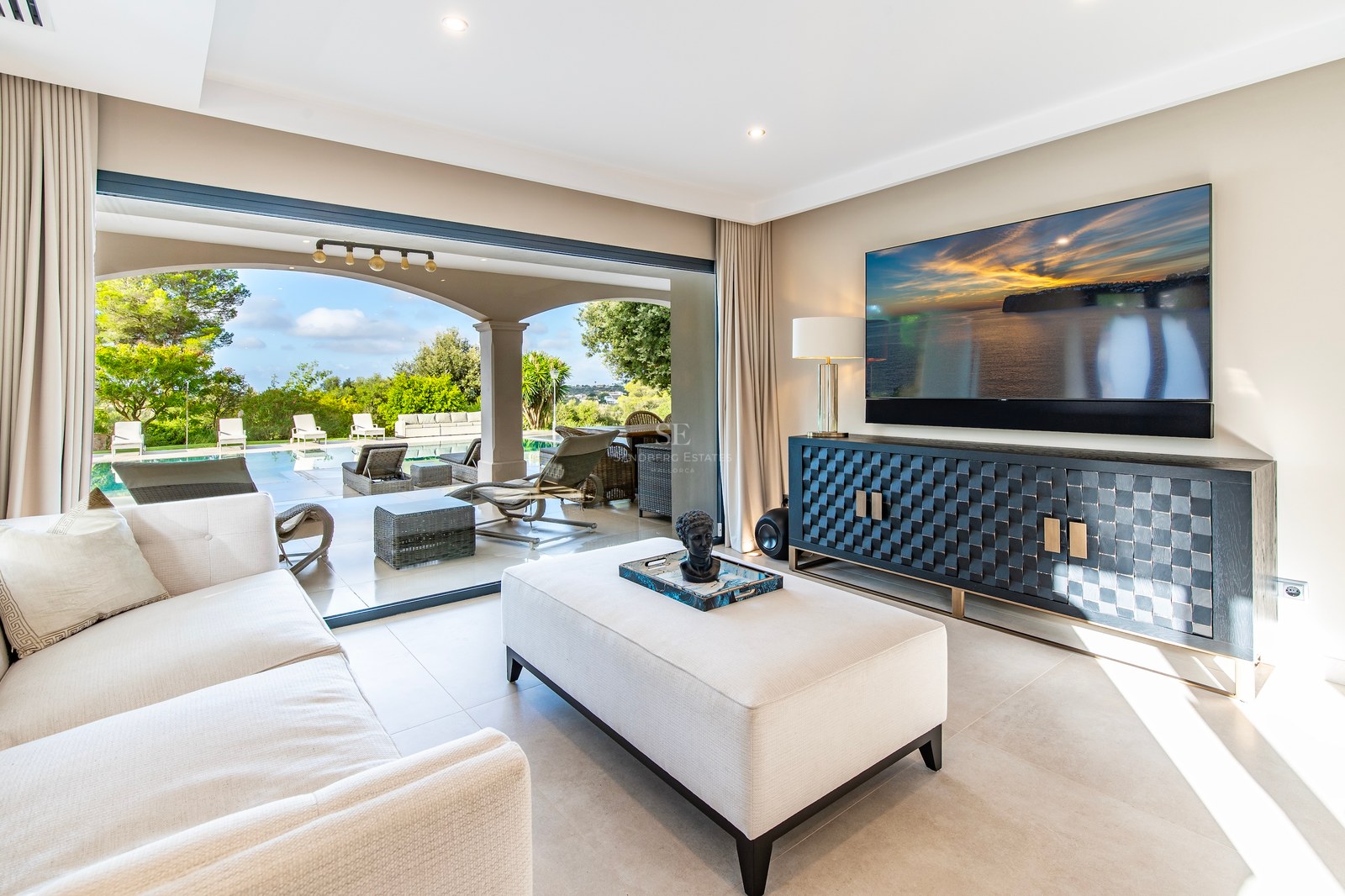 Amplio salón moderno con sofá crema, aparador de diseño y grandes ventanales que dan a la piscina y terraza.