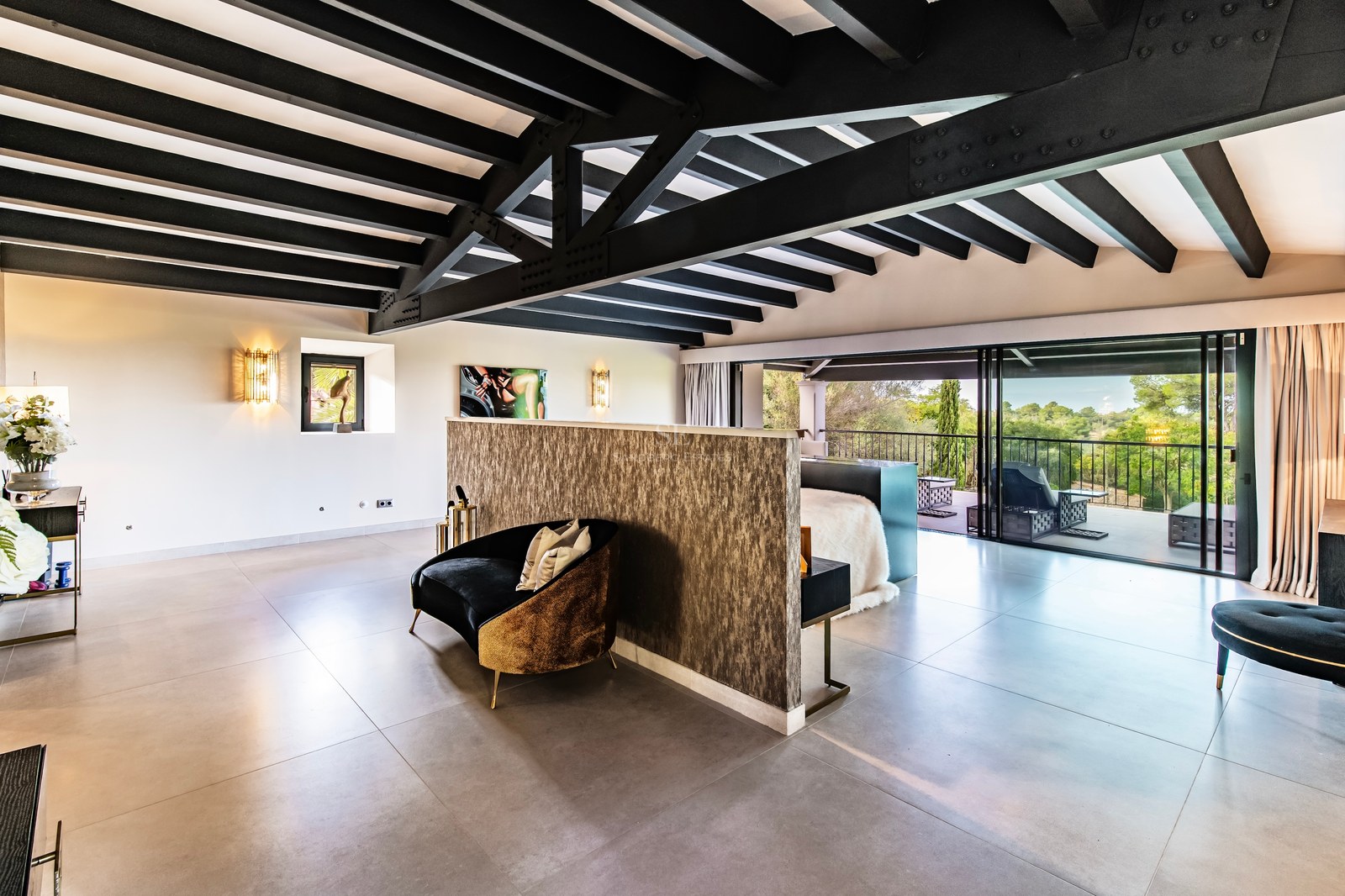 Dormitorio principal moderno con vigas oscuras, terraza privada y muebles de diseño bajo luz natural.