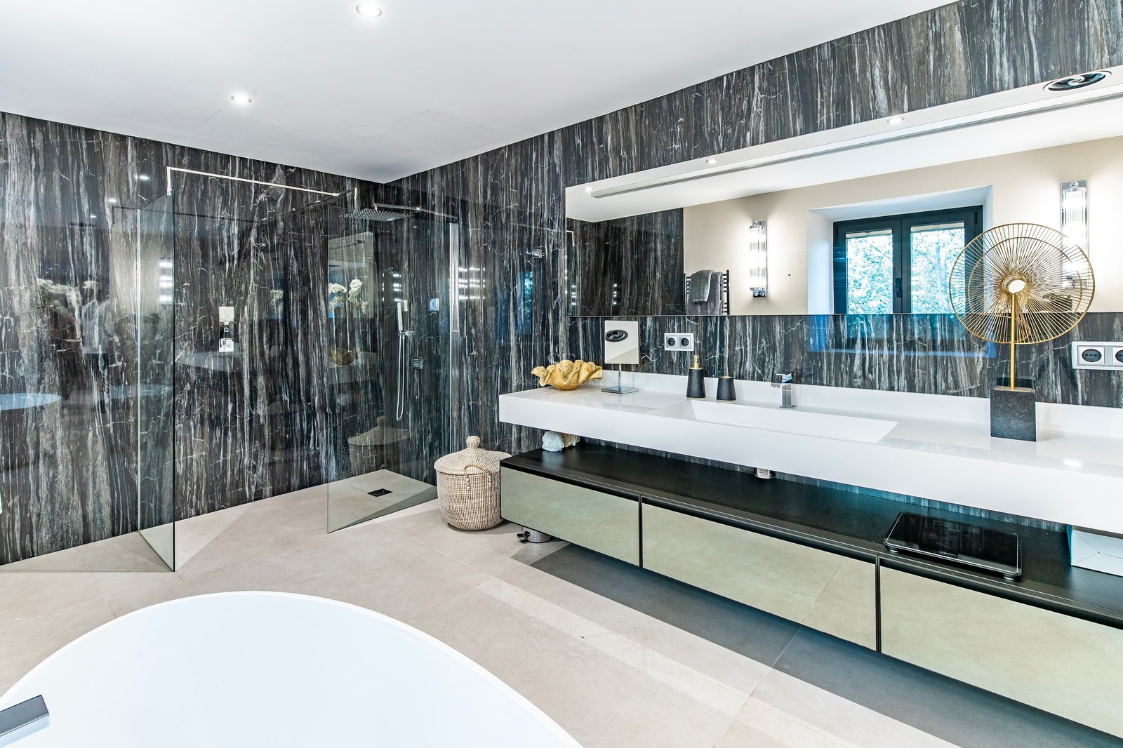 Baño de lujo con paredes de mármol oscuro, ducha de obra acristalada y lavabo doble suspendido.