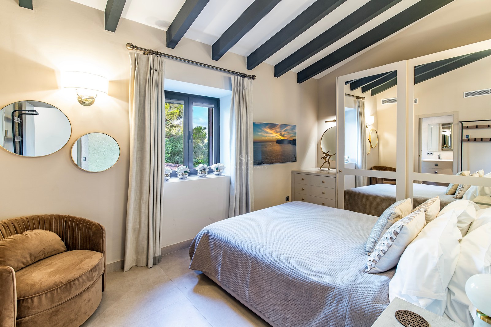 Dormitorio con cama doble, vigas de madera oscura, armario de espejos y ventana con vistas al jardín.