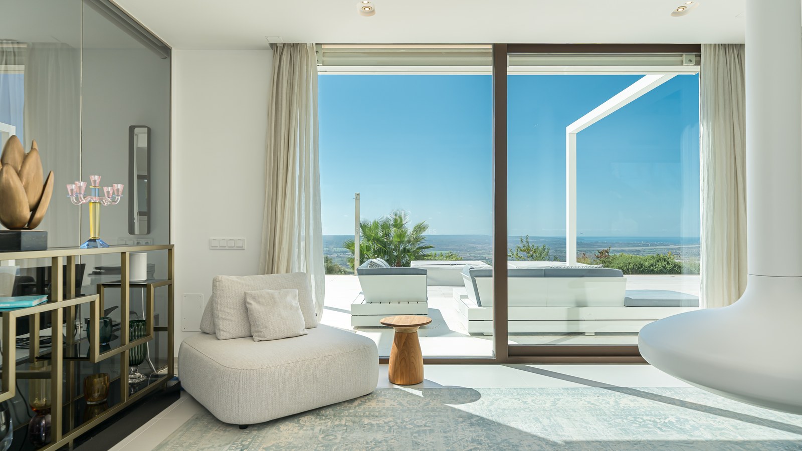 Luminoso salón con ventanales al mar, suelos de madera clara y mobiliario moderno en tonos neutros. Diseño elegante y vistas panorámicas.