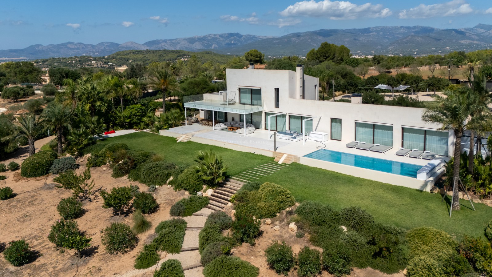 Vista exterior de villa moderna con piscina infinita, amplios ventanales y jardines exuberantes. Arquitectura minimalista.