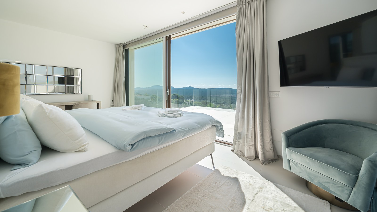 Vista exterior de una villa moderna con piscina infinita, amplias ventanas y arquitectura minimalista. Jardín exuberante y cielo despejado.