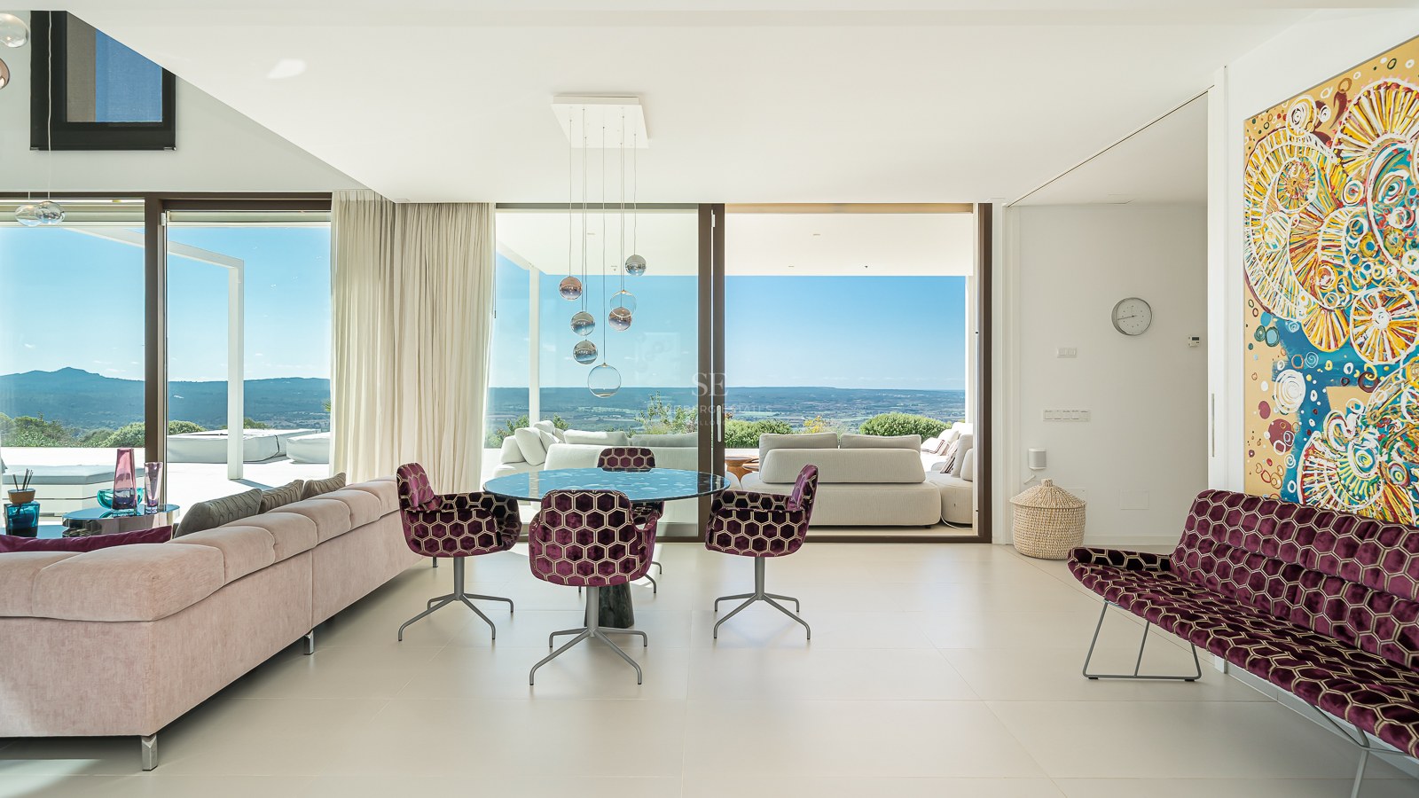 Salon moderne avec chaises en velours violet et larges baies vitrées donnant sur une vallée et la côte.