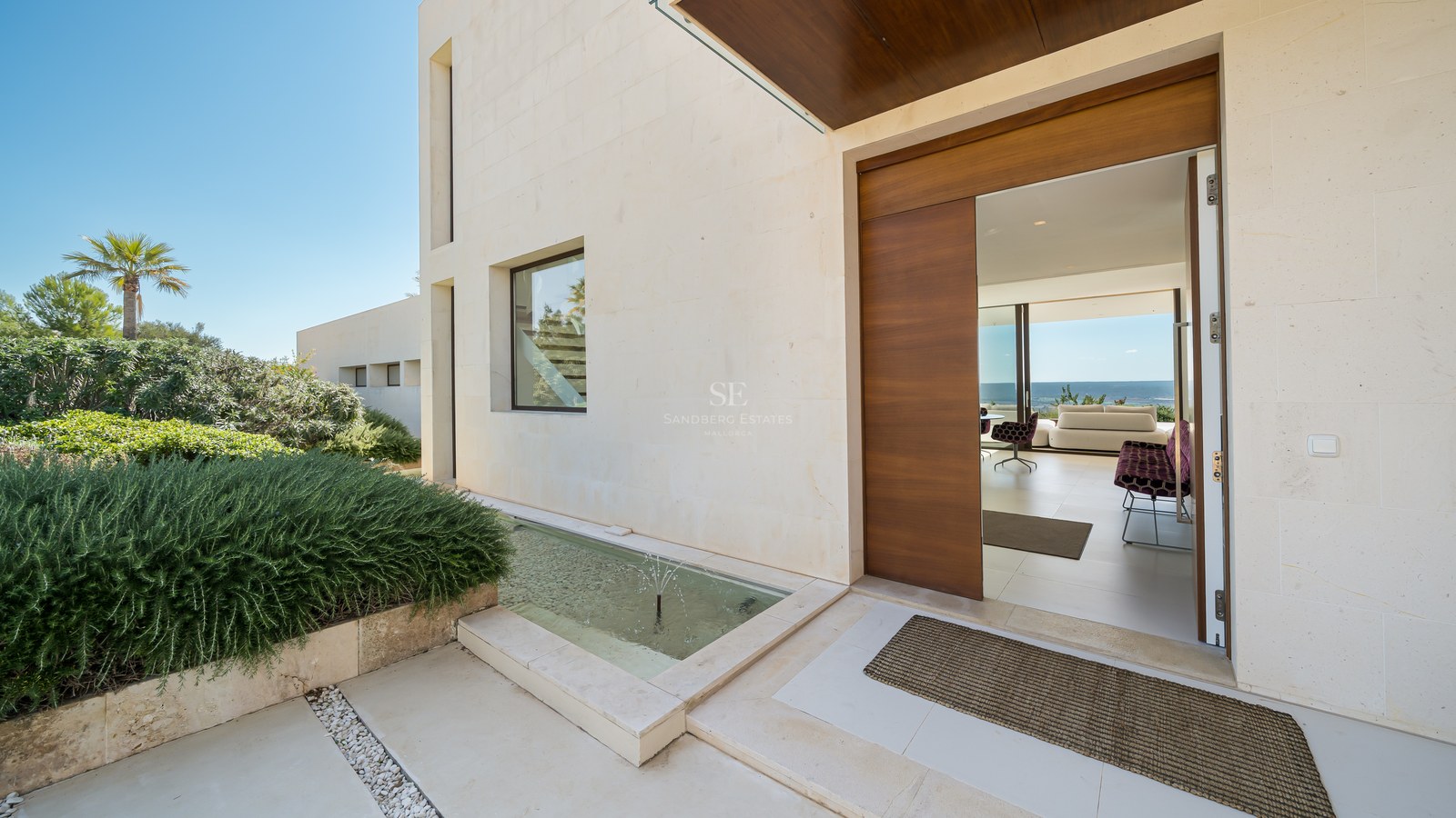 Vista exterior de una moderna casa con piscina, amplios ventanales, terraza de madera y exuberante vegetación. Arquitectura minimalista.