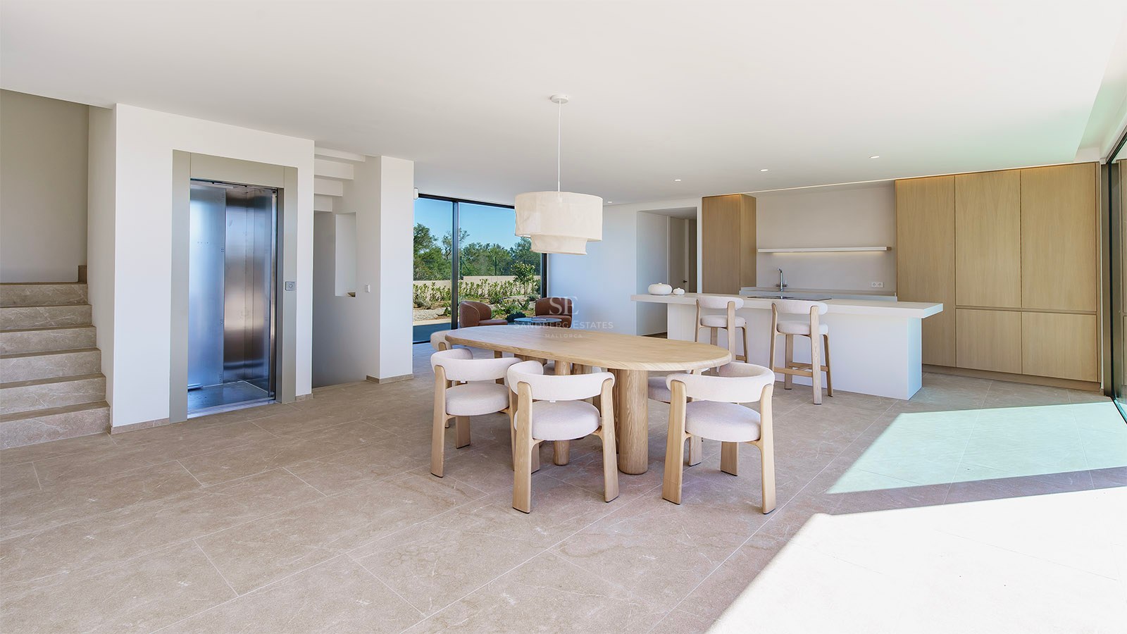 Salle à manger lumineuse avec table ovale en bois, chaises blanches et baies vitrées donnant sur le jardin.