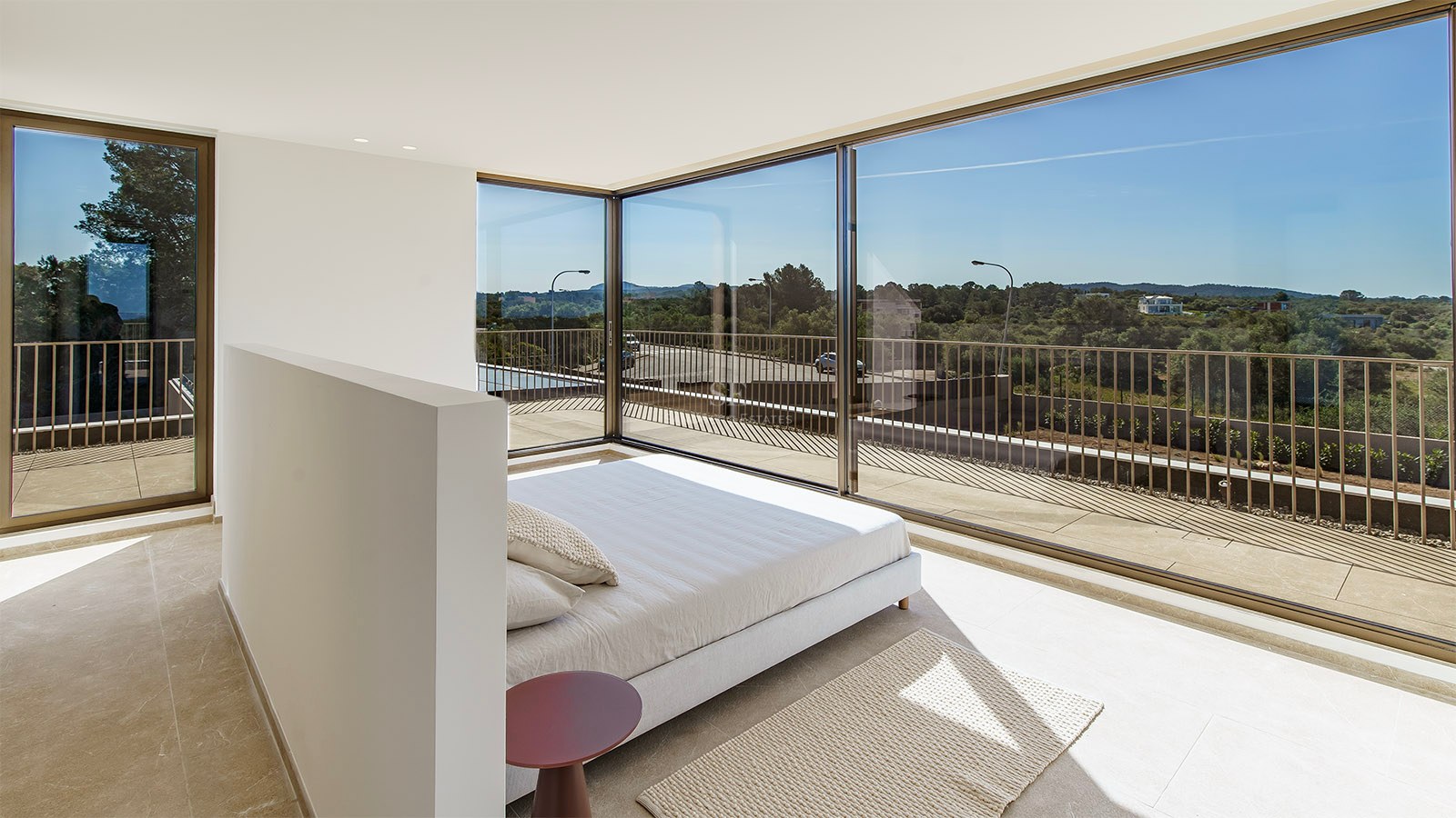 Chambre minimaliste avec baies vitrées toute hauteur offrant une vue sur le paysage verdoyant et la terrasse.