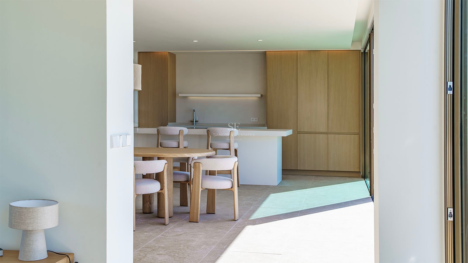 Cuisine moderne lumineuse avec placards en chêne clair, îlot en pierre blanche et table à manger circulaire en bois.