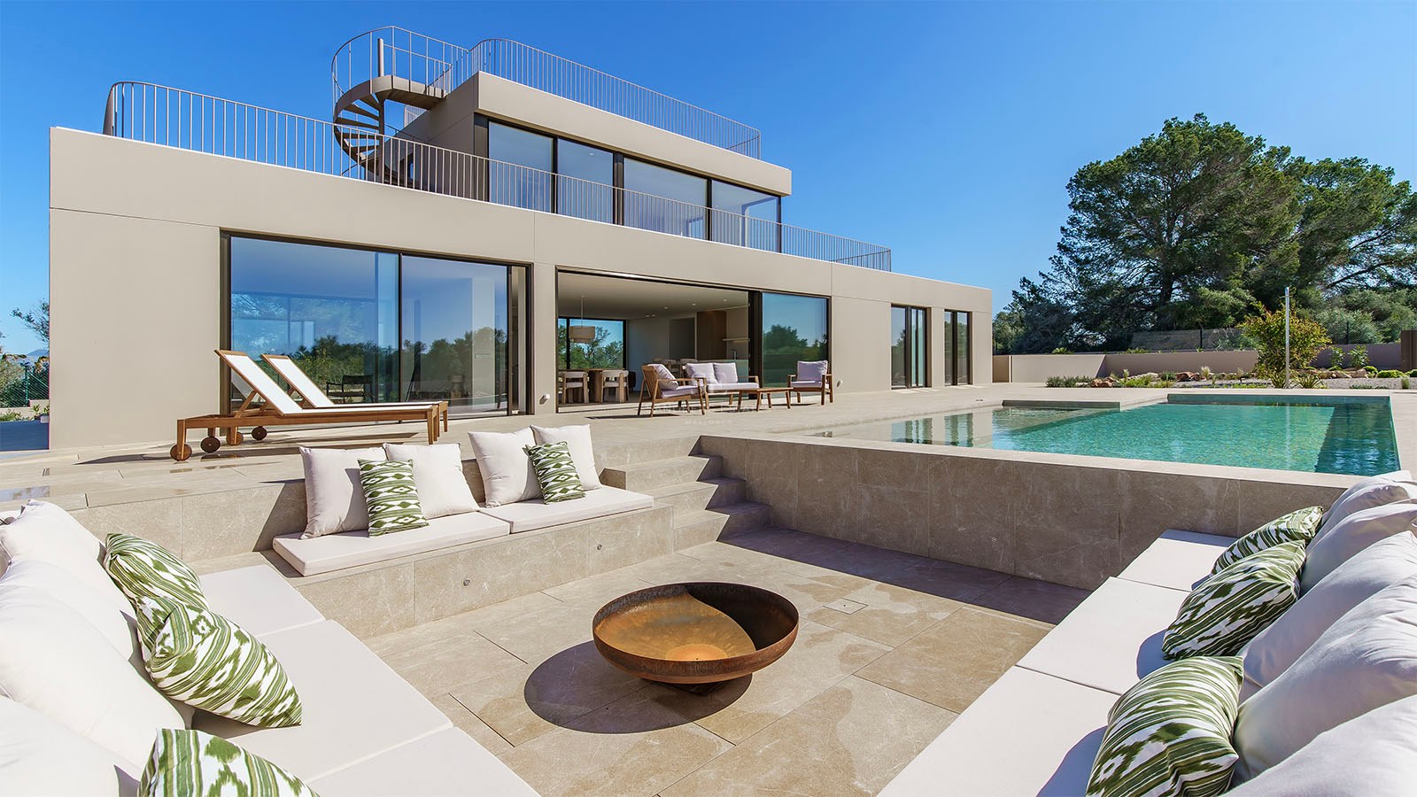 Extérieur d'une villa moderne à deux étages avec un salon encastré et un brasero à côté d'une piscine turquoise.