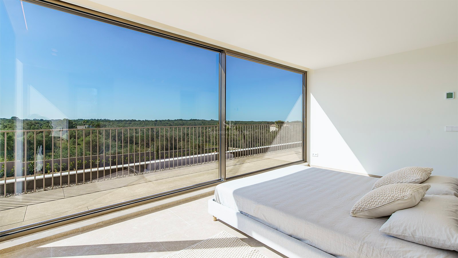 Chambre principale lumineuse avec de grandes baies vitrées coulissantes ouvrant sur une terrasse surplombant la nature.