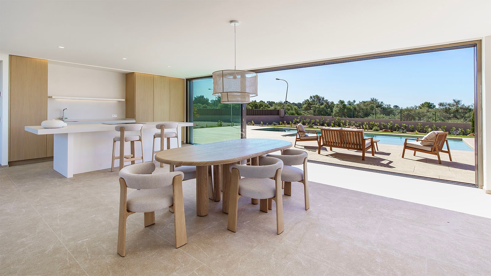 Espace dînatoire en bois clair avec baies vitrées ouvertes sur une terrasse et une piscine ensoleillée.