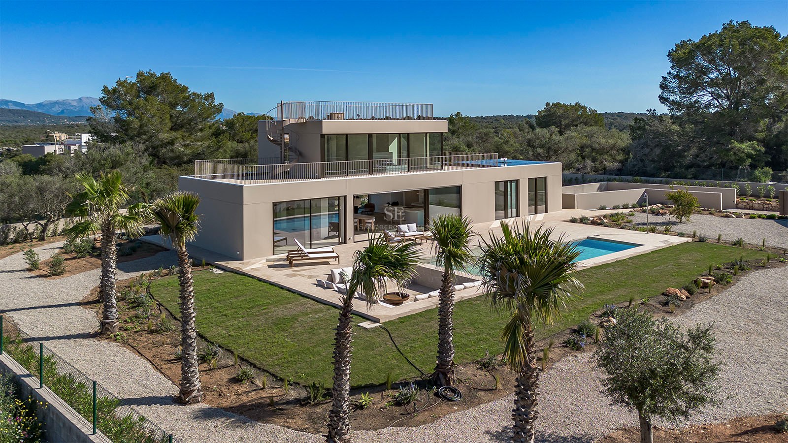 Vue d'une villa contemporaine à deux étages avec piscine, pelouse et balcons en verre sous un ciel bleu.