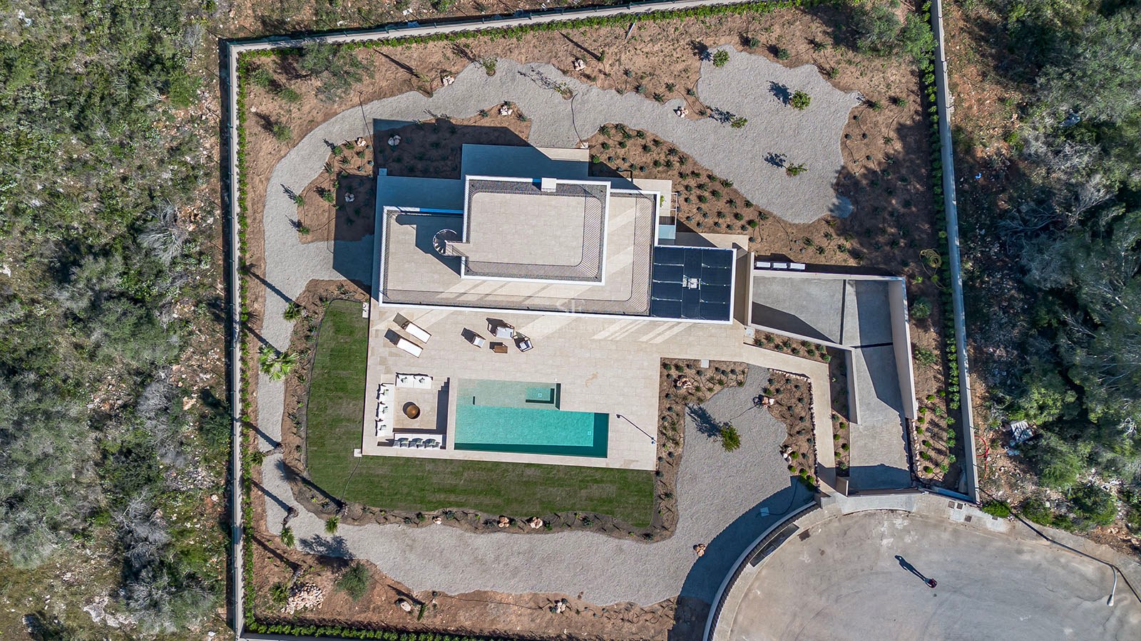 Vue par drone d'une villa contemporaine avec piscine rectangulaire, jardin paysager et terrasse géométrique.