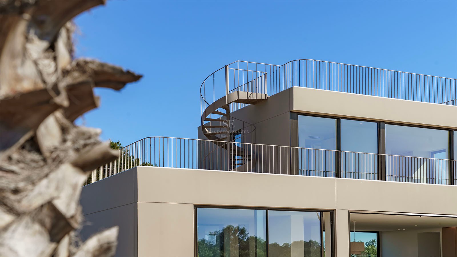 Détail architectural d'une villa beige contemporaine avec un escalier en colimaçon menant au toit sous un ciel dégagé.