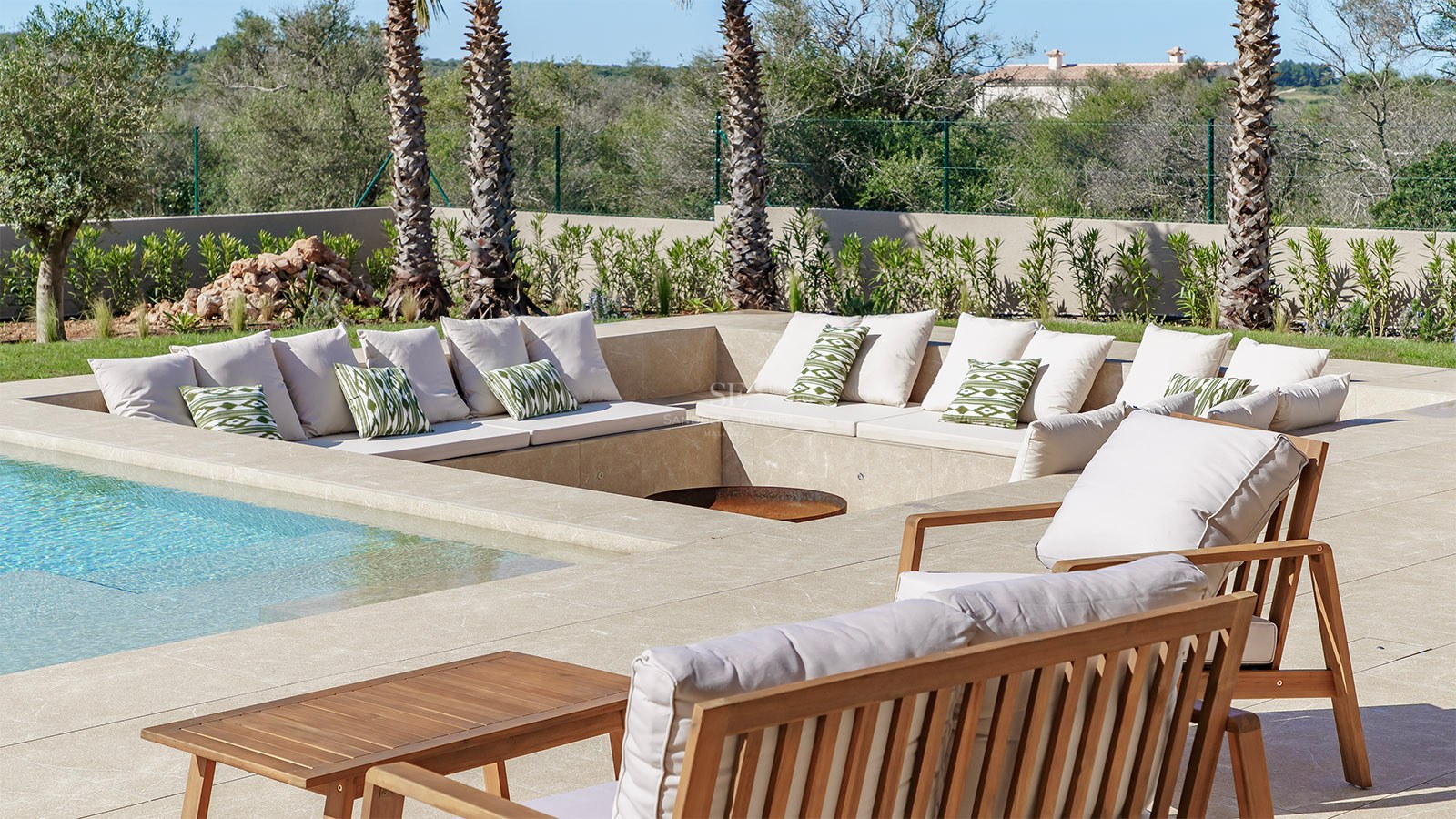Salon d'été encastré en pierre naturelle avec mobilier en bois à côté d'une piscine et de palmiers.