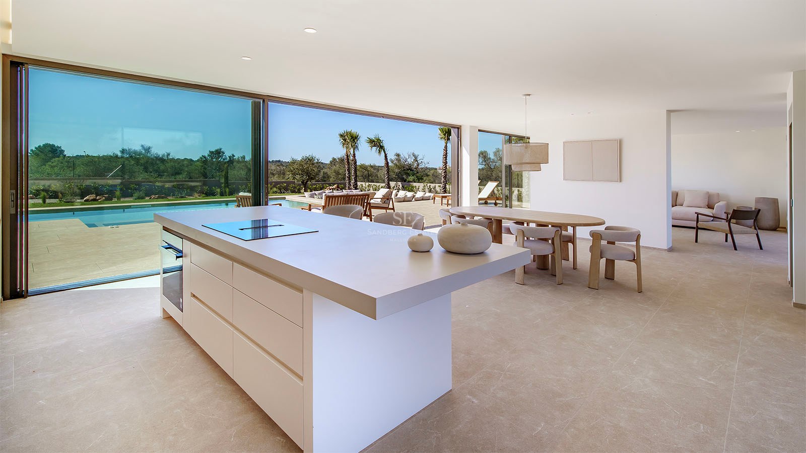 Îlot de cuisine moderne et salle à manger avec baies vitrées s'ouvrant sur une terrasse ensoleillée avec piscine.