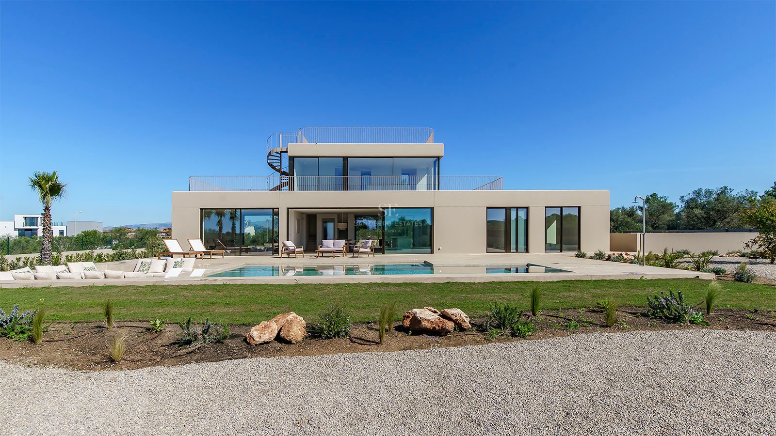 Villa moderne de deux étages avec grande piscine rectangulaire, baies vitrées et escalier extérieur en colimaçon.