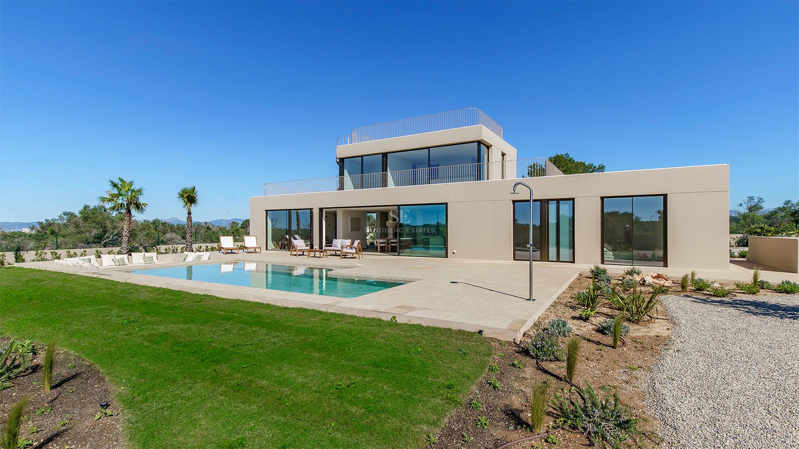 Façade d'une villa moderne de deux étages avec de grandes baies vitrées, piscine privée et jardin sous un ciel bleu.