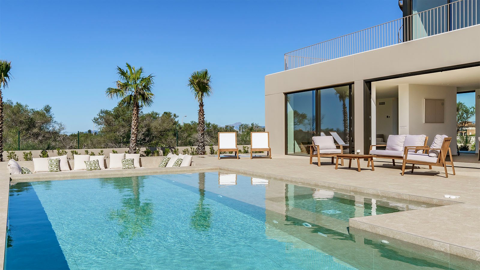 Piscine moderne turquoise avec terrasse en pierre, chaises longues de design et palmiers sous un ciel bleu clair.