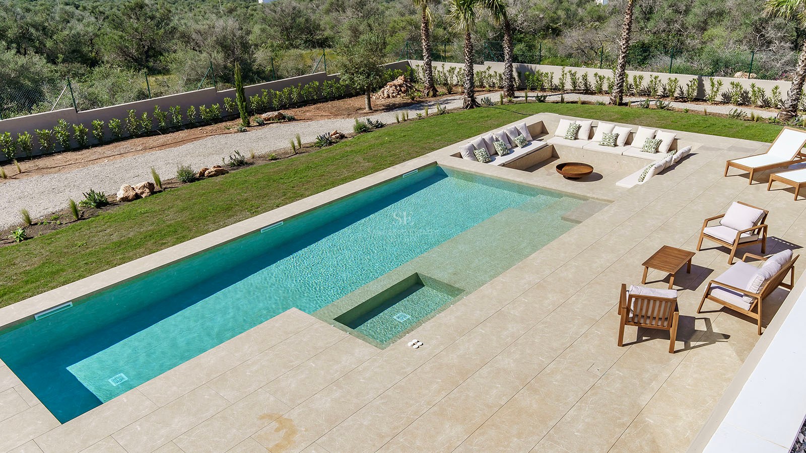 Piscine rectangulaire turquoise avec terrasse en pierre naturelle et coin salon encastré avec coussins et brasero.