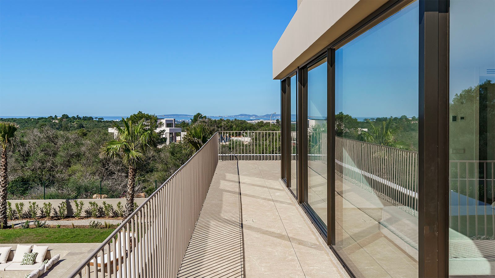 Balcon contemporain avec baies vitrées, garde-corps métallique et vue mer sous un ciel bleu clair.