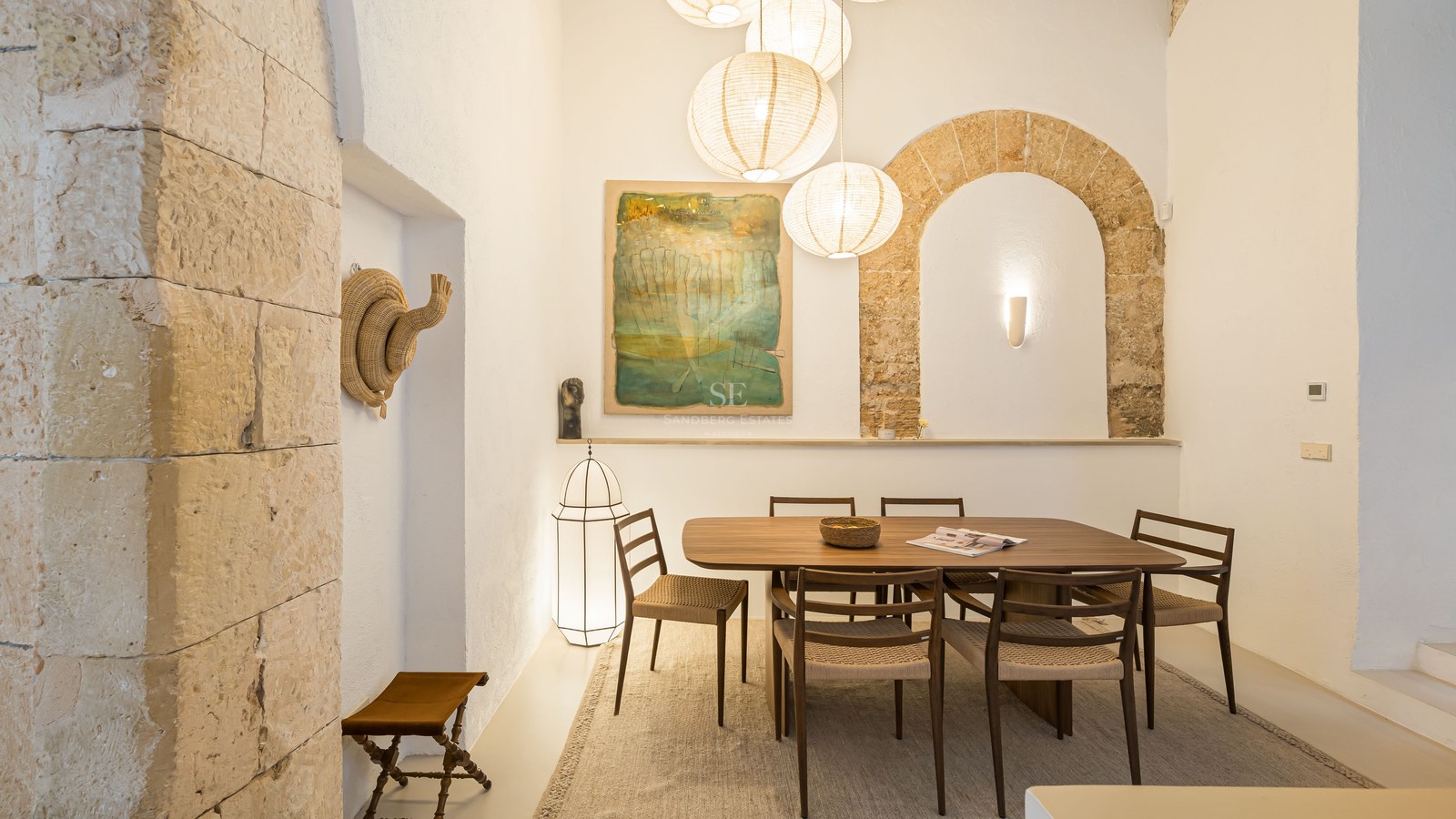 Salle à manger minimaliste avec table en bois sombre, arche en pierre et grandes suspensions en papier.