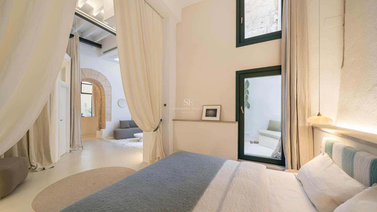 Chambre contemporaine avec une arche en pierre, de hauts plafonds, de grands rideaux crème et une décoration minimaliste.