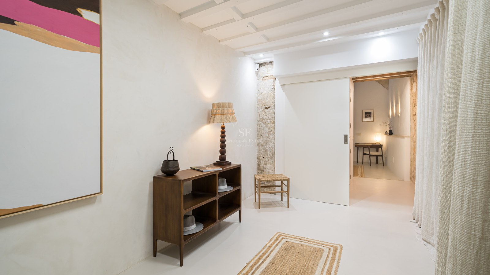 Hall d'entrée moderne avec buffet en bois foncé, mur en pierre apparente, plafond à poutres blanches et porte coulissante.
