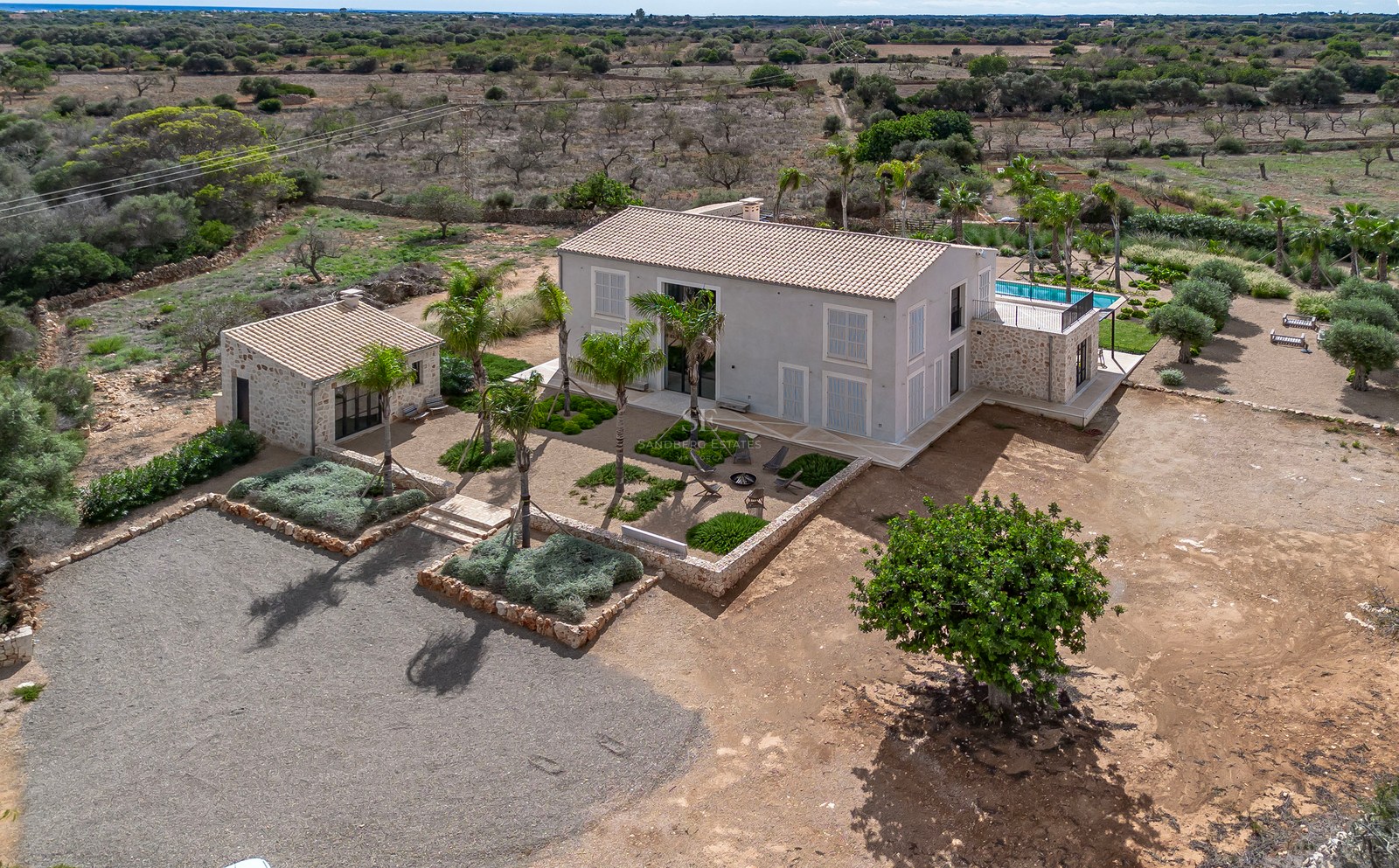 Vue aérienne d'une villa contemporaine beige avec piscine et jardin paysager dans la campagne majorquine.