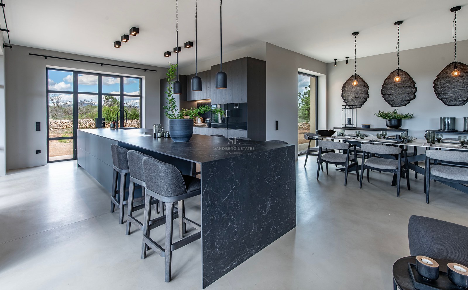 Cuisine ouverte moderne avec îlot en marbre noir, tabourets gris et espace salle à manger sous des suspensions design.
