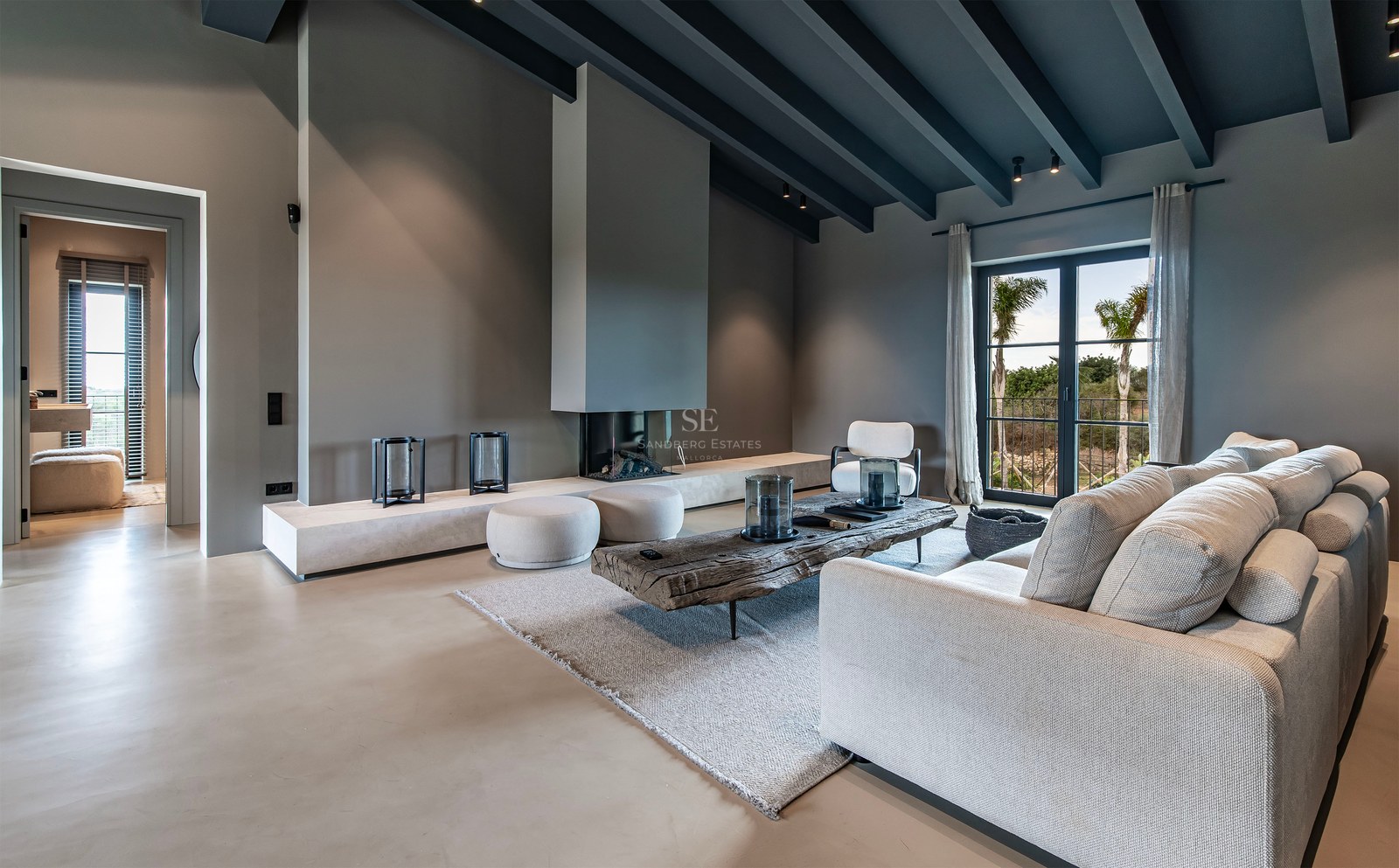 Grand salon moderne avec poutres grises, canapé beige, table en bois rustique et cheminée intégrée minimaliste.