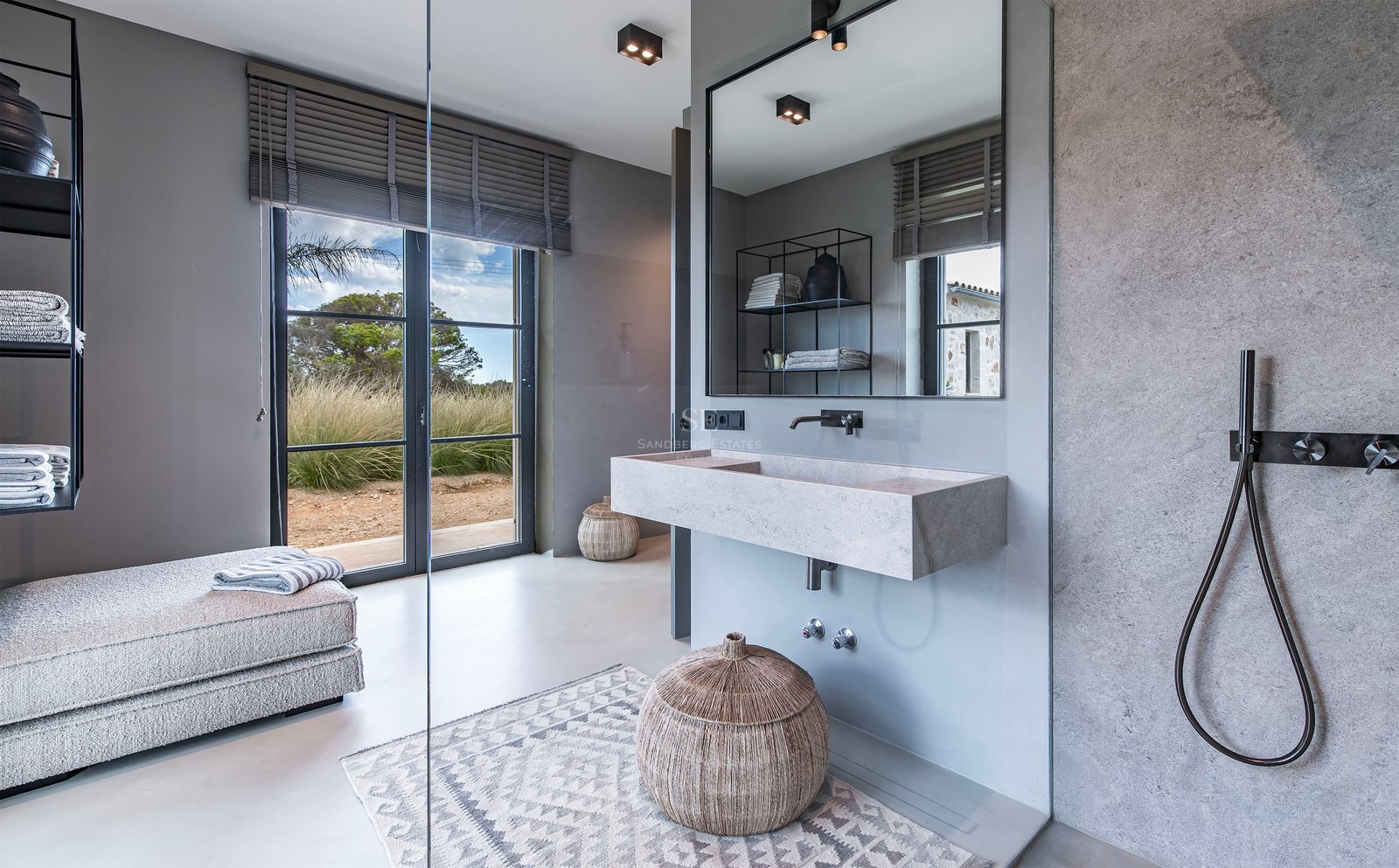 Salle de bains moderne avec vasque suspendue en pierre, robinetterie noir mat et porte vitrée donnant sur le jardin.