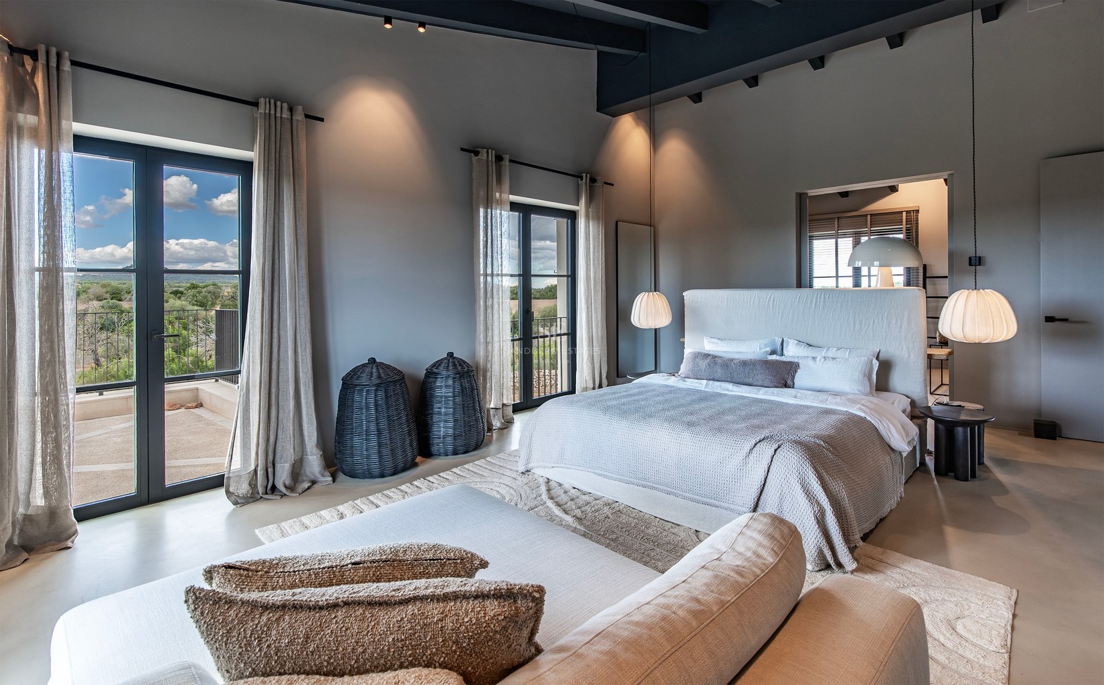 Chambre principale contemporaine avec poutres apparentes, grand lit et portes-fenêtres ouvrant sur un balcon avec vue.