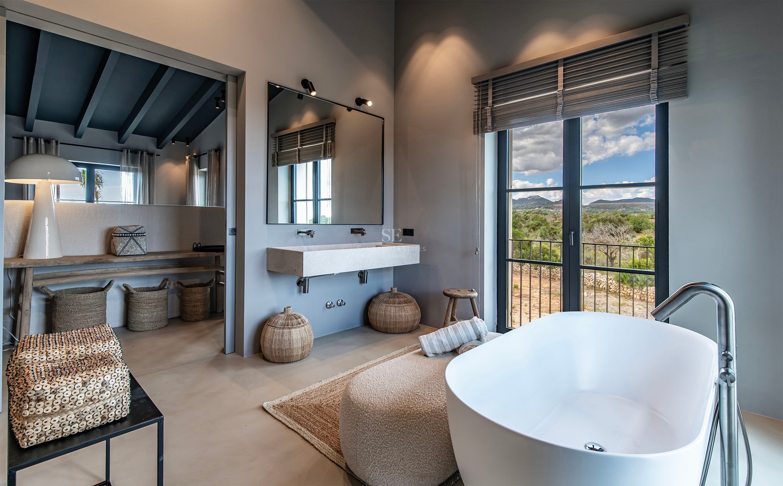 Salle de bain moderne avec baignoire îlot, lavabo suspendu et grande fenêtre donnant sur un paysage de montagne.